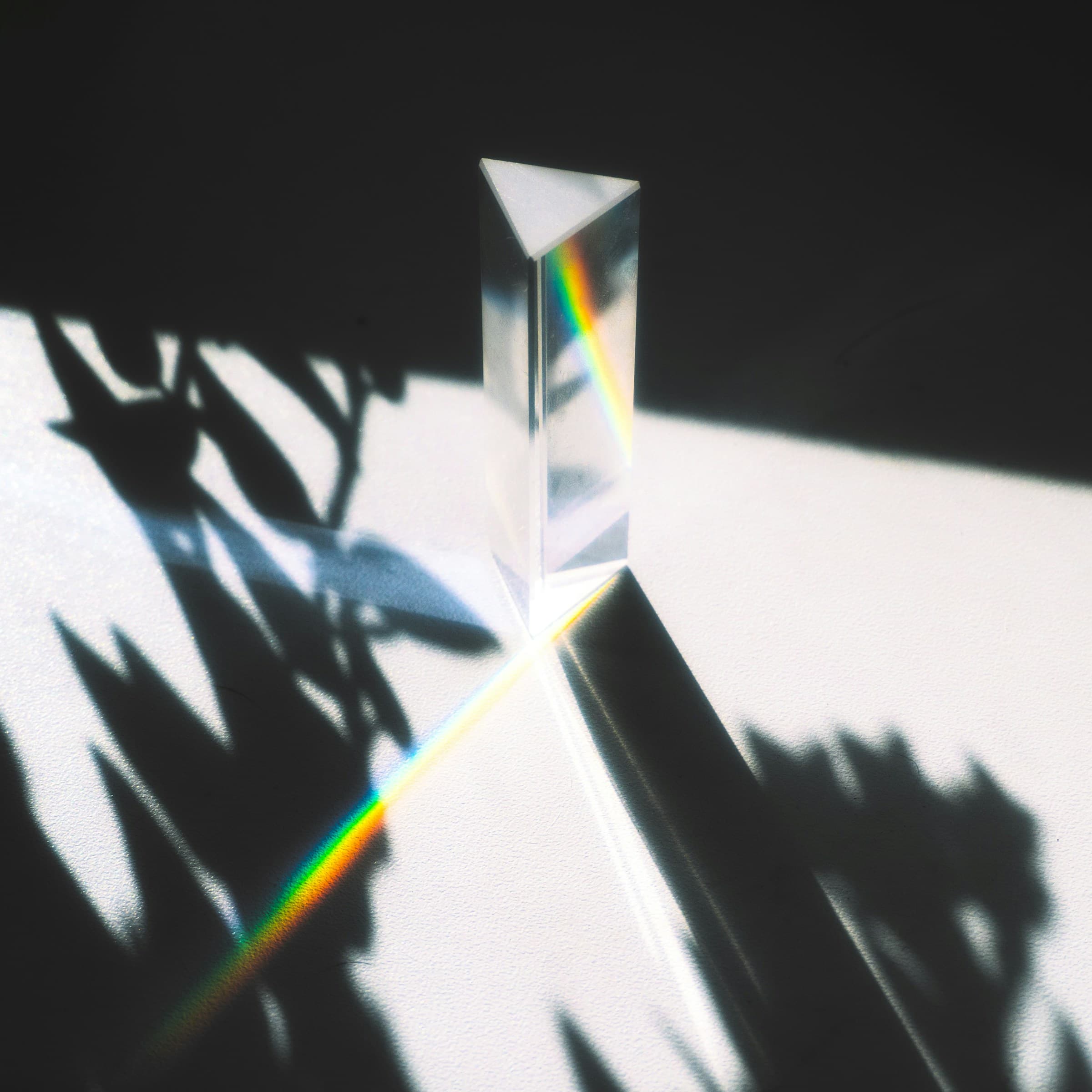 A glass prism splitting sunlight into a spectrum on a bright surface